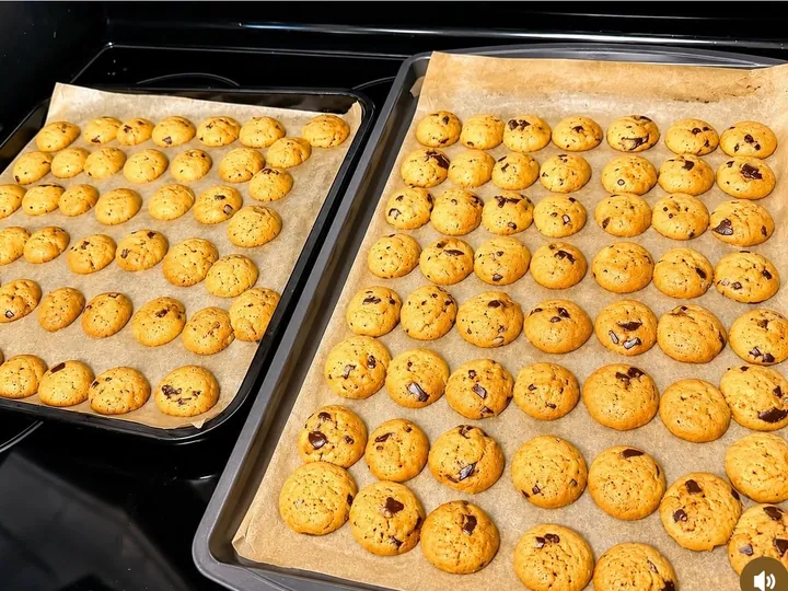 Trays of freshly baked mini chocolate chip cookies cooling on parchment.