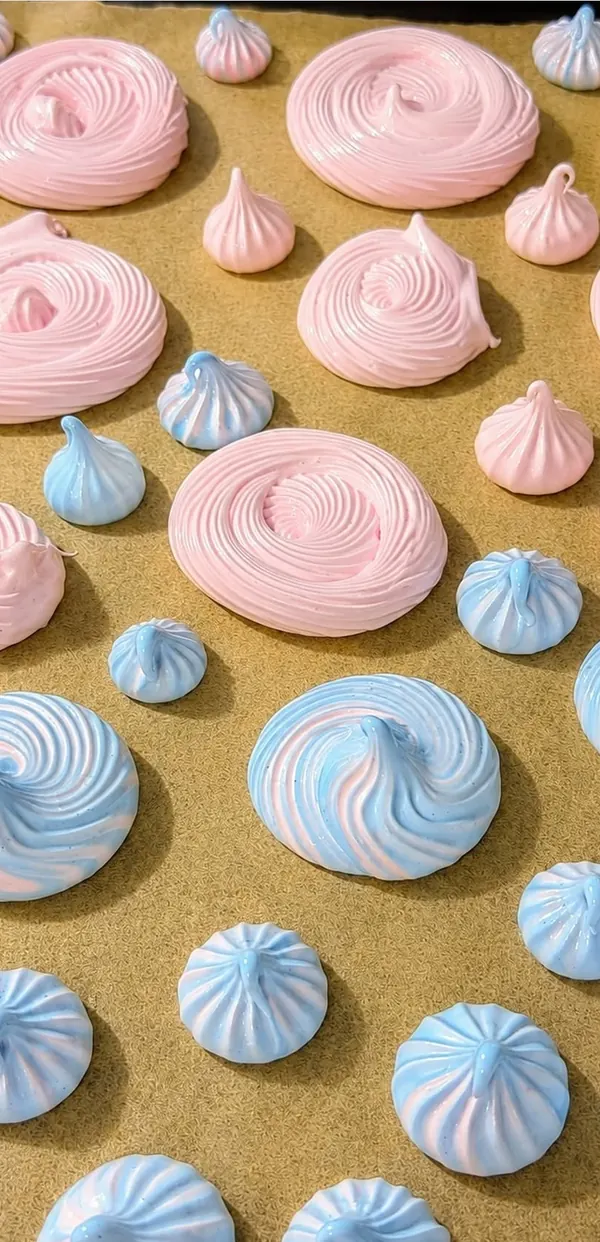 Pink and blue meringue cookies arranged on a baking tray.