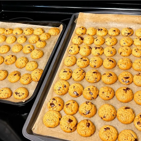 Mini chocolate chip cookies cooling on a parchment-lined sheet pan.