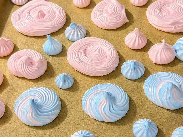 Pink and blue swirled meringue cookies piped onto a baking sheet.